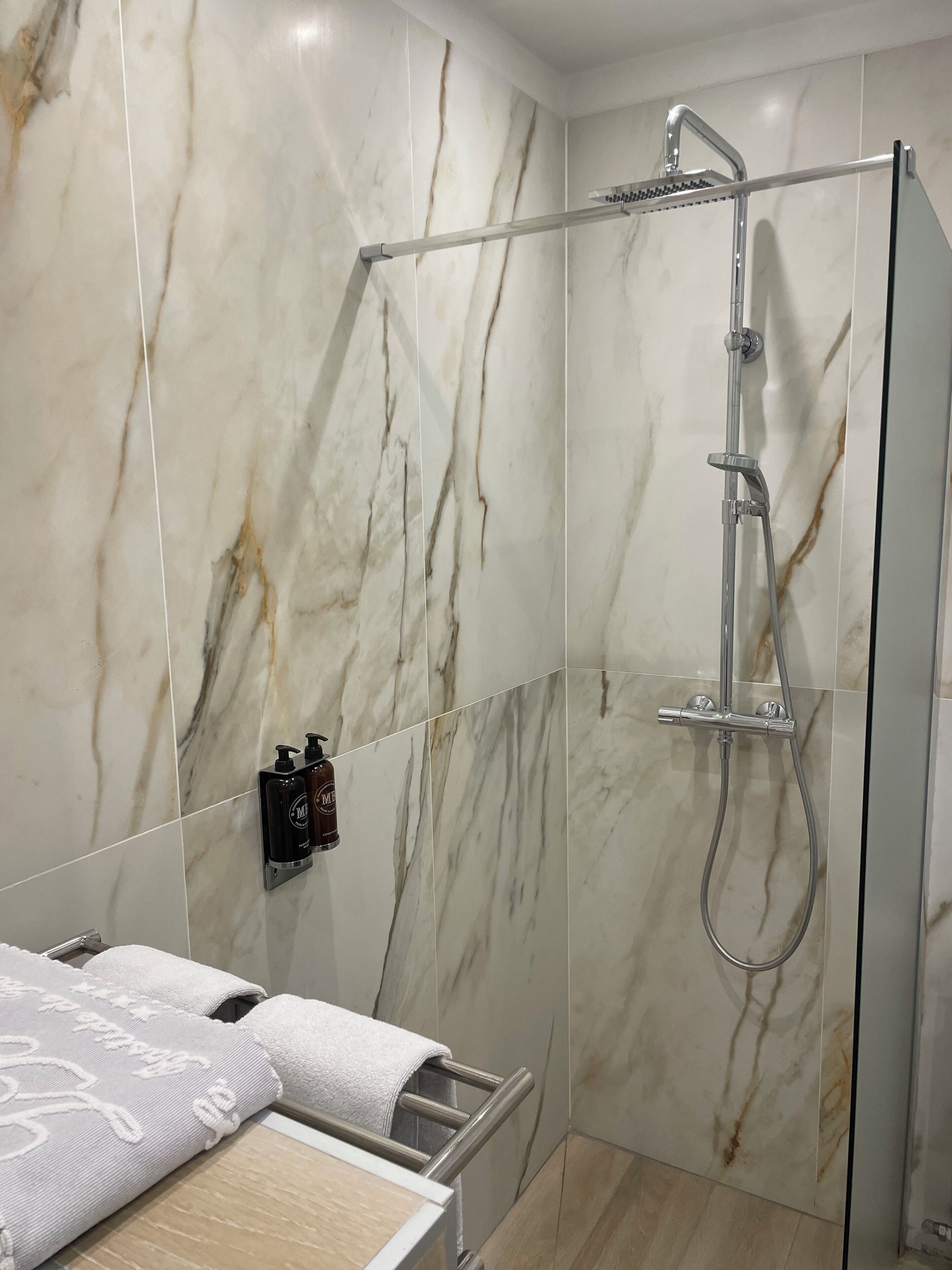 Une salle de bain moderne avec des murs en marbre, une douche en verre et un porte-serviettes.