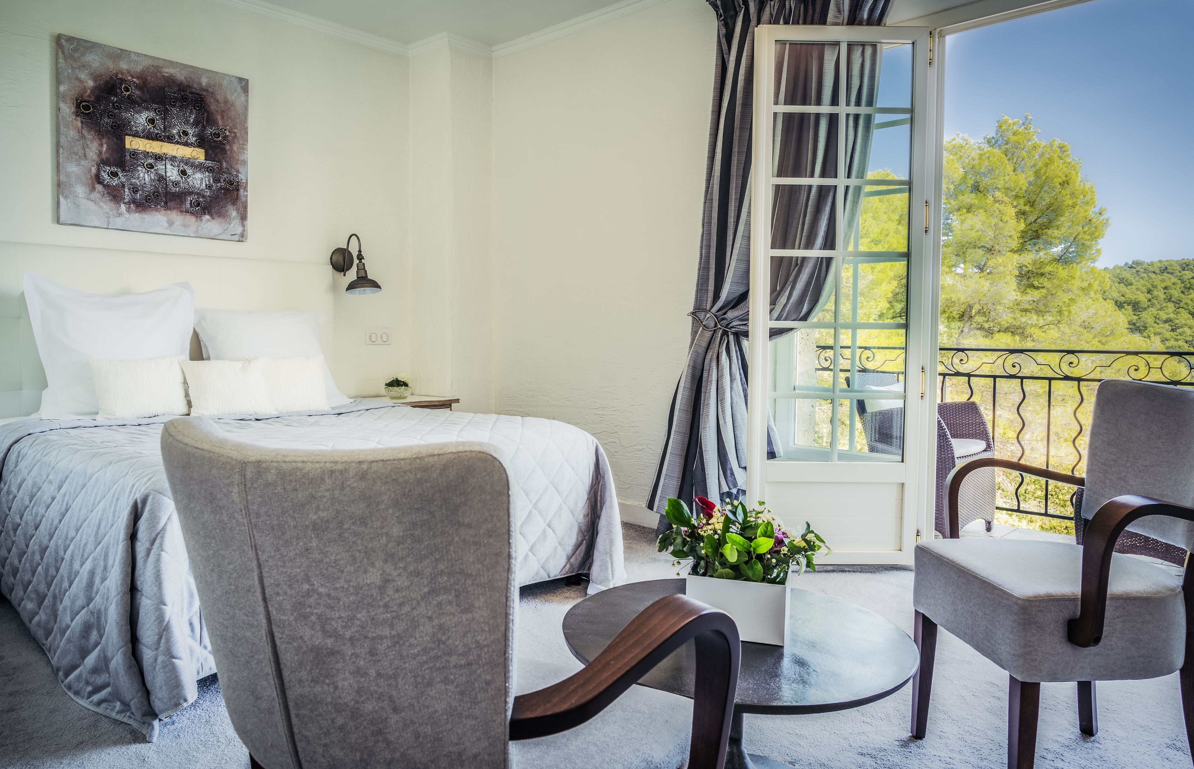 Un dormitorio con cama, dos sillas, una mesita y una ventana con cortinas.