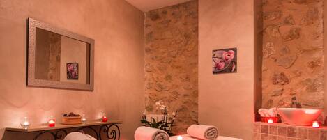 Un cuarto de spa con una camilla de masaje, velas, una pared de piedra y una pequeña chimenea.