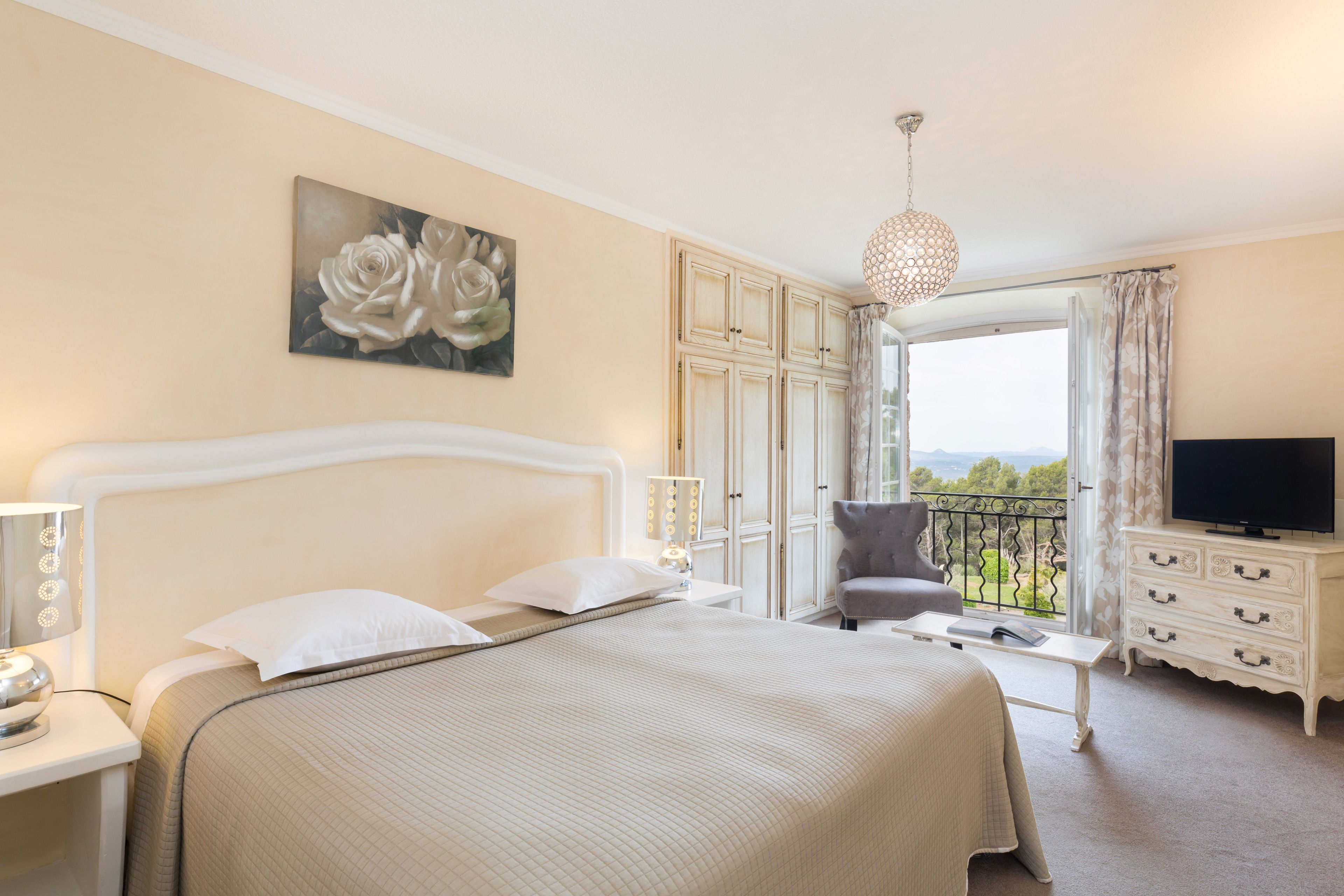 Habitación de hotel con una cama grande, televisión, balcón con vistas y un cuadro en la pared.