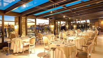 Un restaurante con mesas redondas, sillas y vistas de la ciudad a través de amplios ventanales.