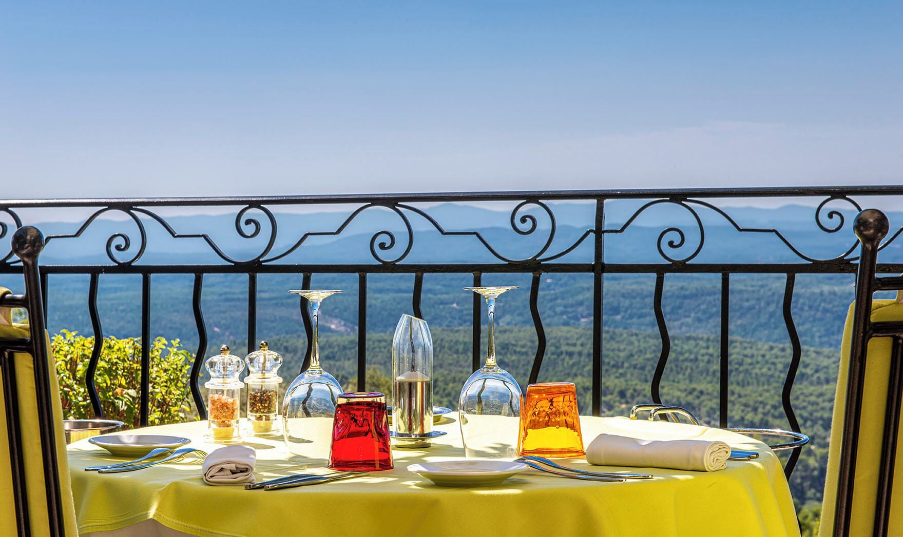 Een gedekte tafel met divers glazuurwerk en servies, met uitzicht op een bergachtig landschap.