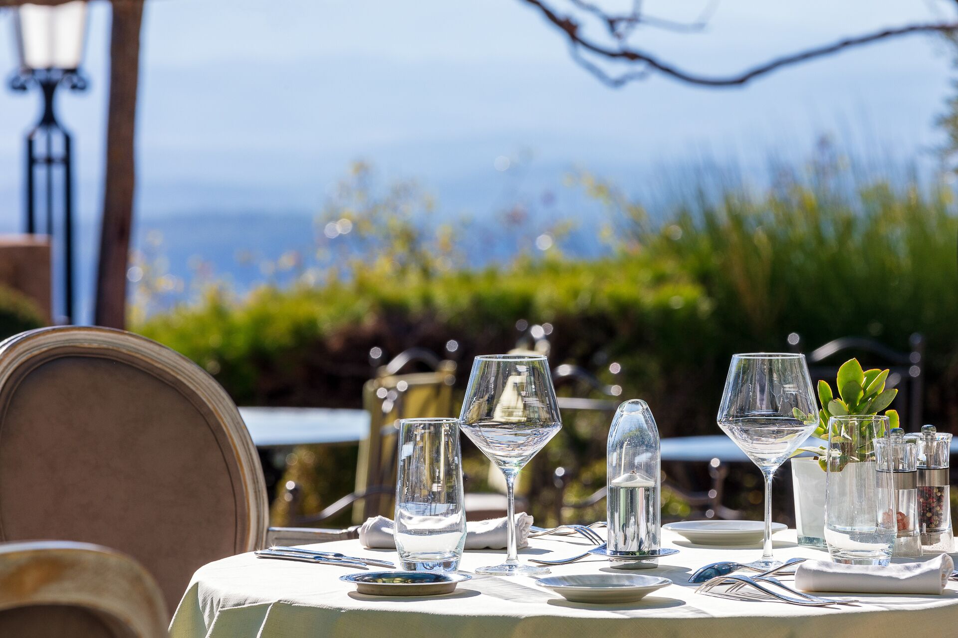 A table set for dining with clear glassware and a view of the sea in the background.