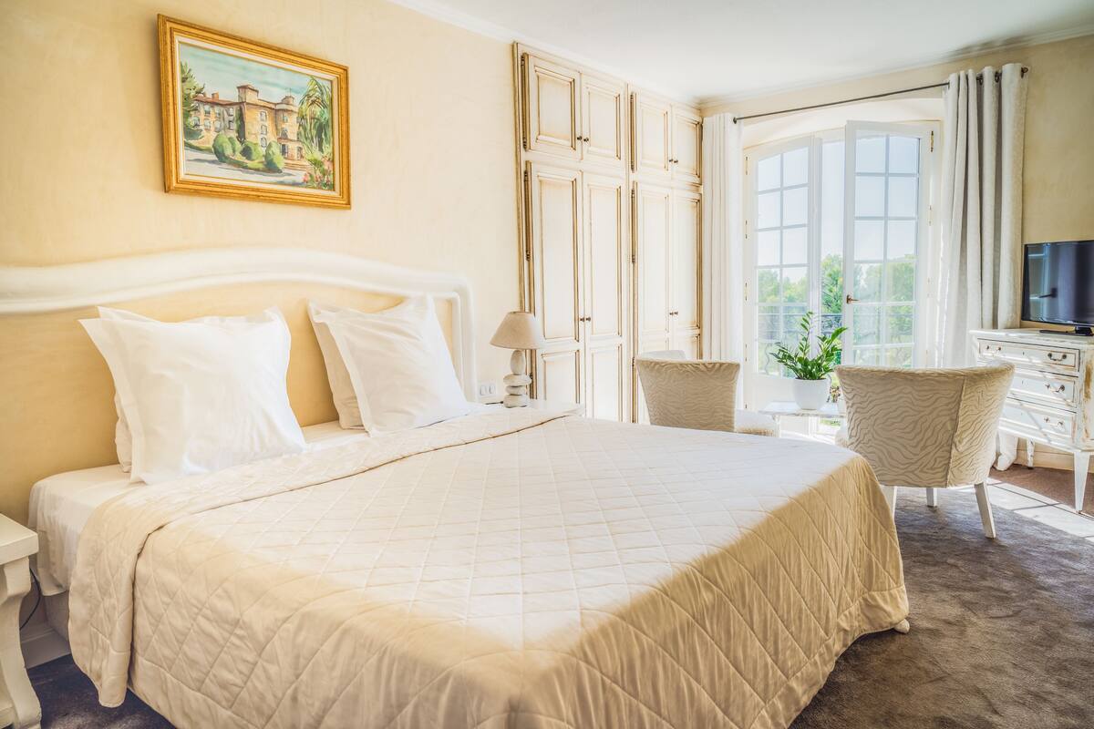 A hotel room with a large bed, a desk with a television, and a window with curtains.