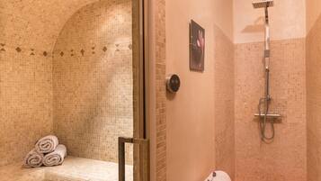 Bathroom features a glass-enclosed shower area and a bench with neatly rolled towels.