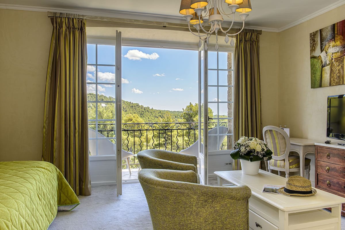 A bedroom with a balcony, a desk, a chair, and a bed.