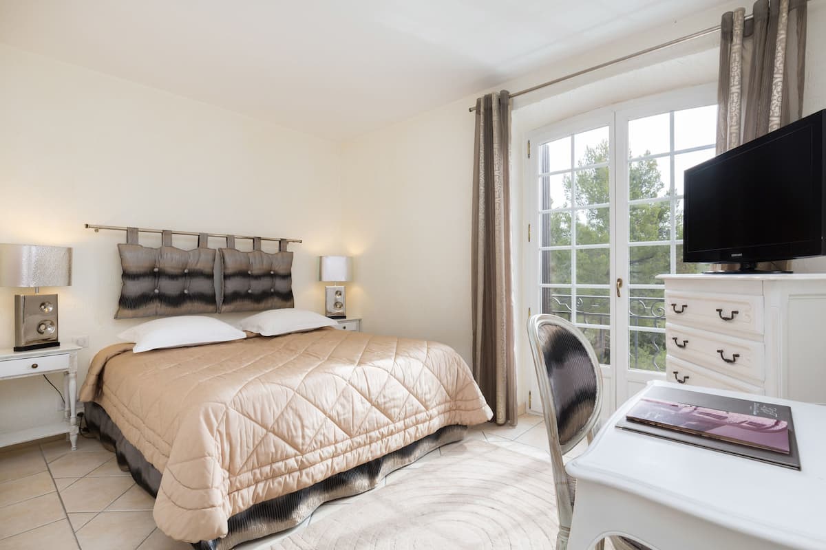 A bedroom with a bed, bedside tables, a TV, a chair, and a window.
