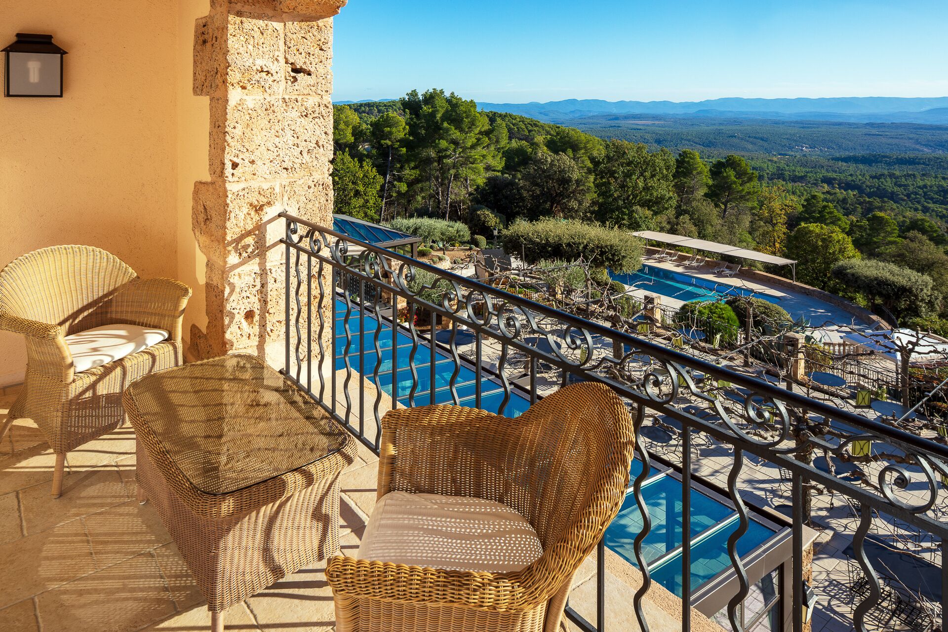 Un balcon doté de meubles en osier, donnant sur une piscine et offrant une vue panoramique sur un paysage boisé.