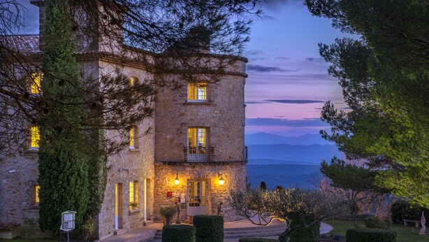 Un edificio de piedra con balcón, un césped cuidado y vistas al mar.