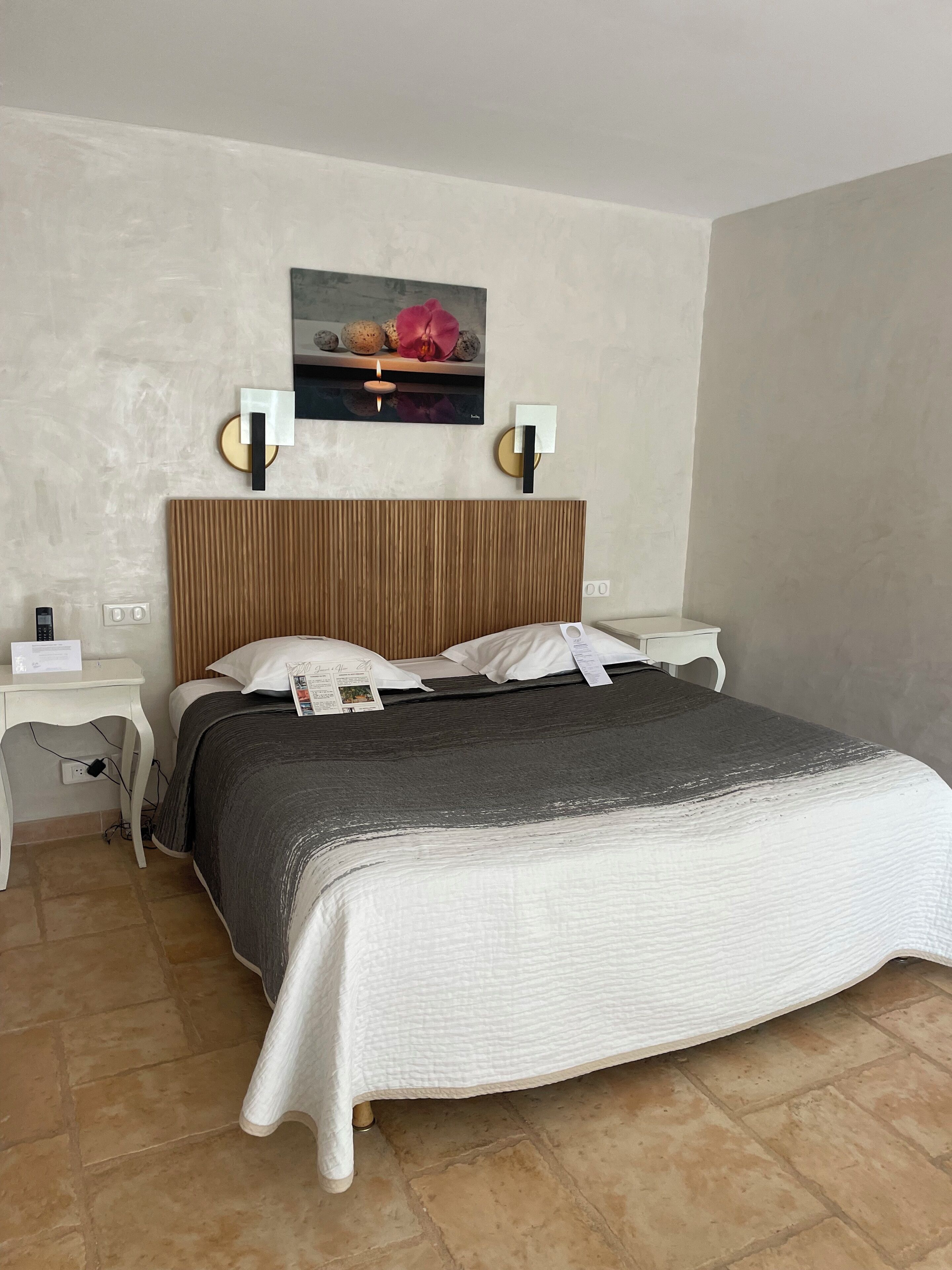 A neatly arranged hotel room with a bed, bedside tables, a wall-mounted artwork, and a simple light fixture.