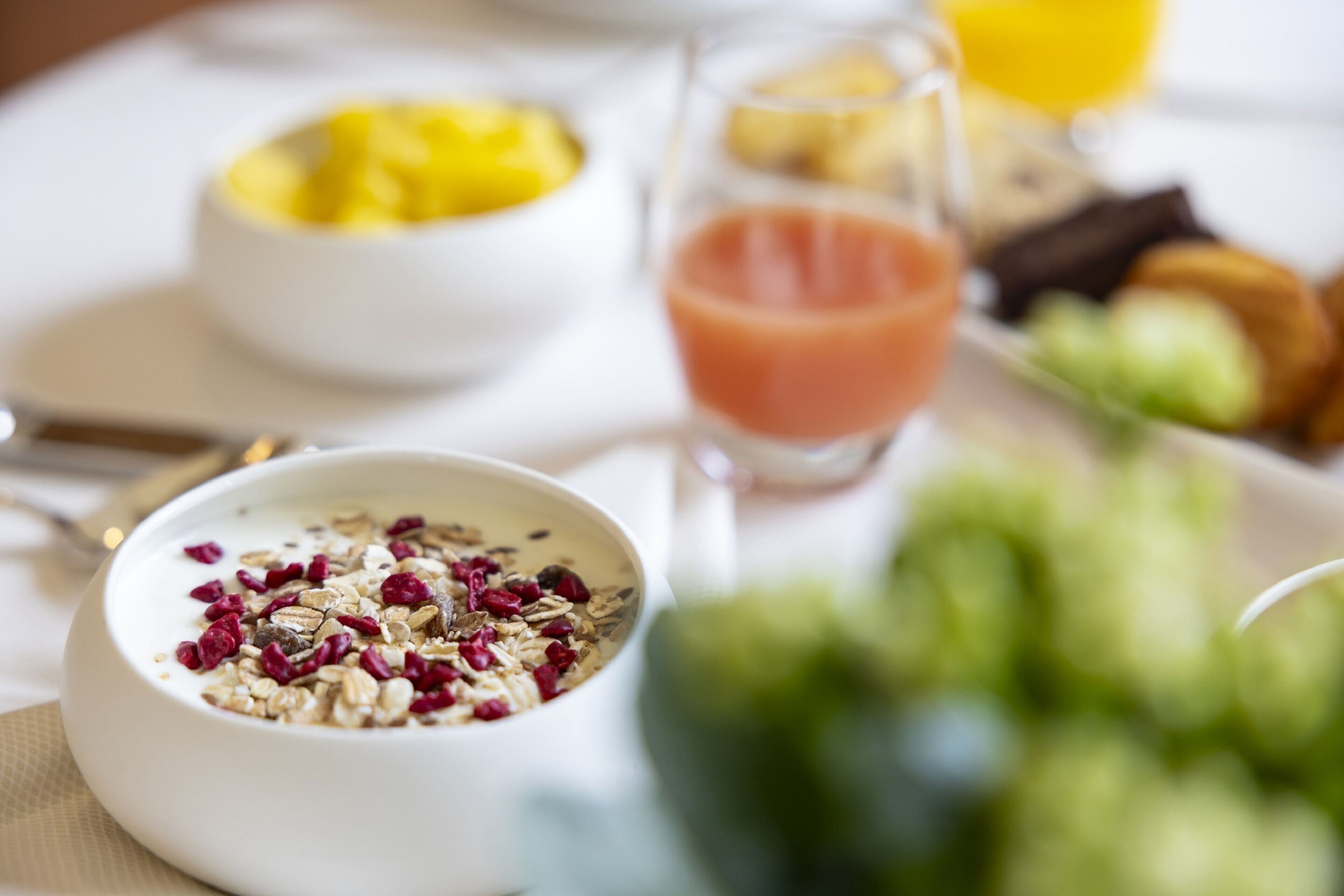 A breakfast setting with a bowl of cereal, a glass of juice, and a plate of food.