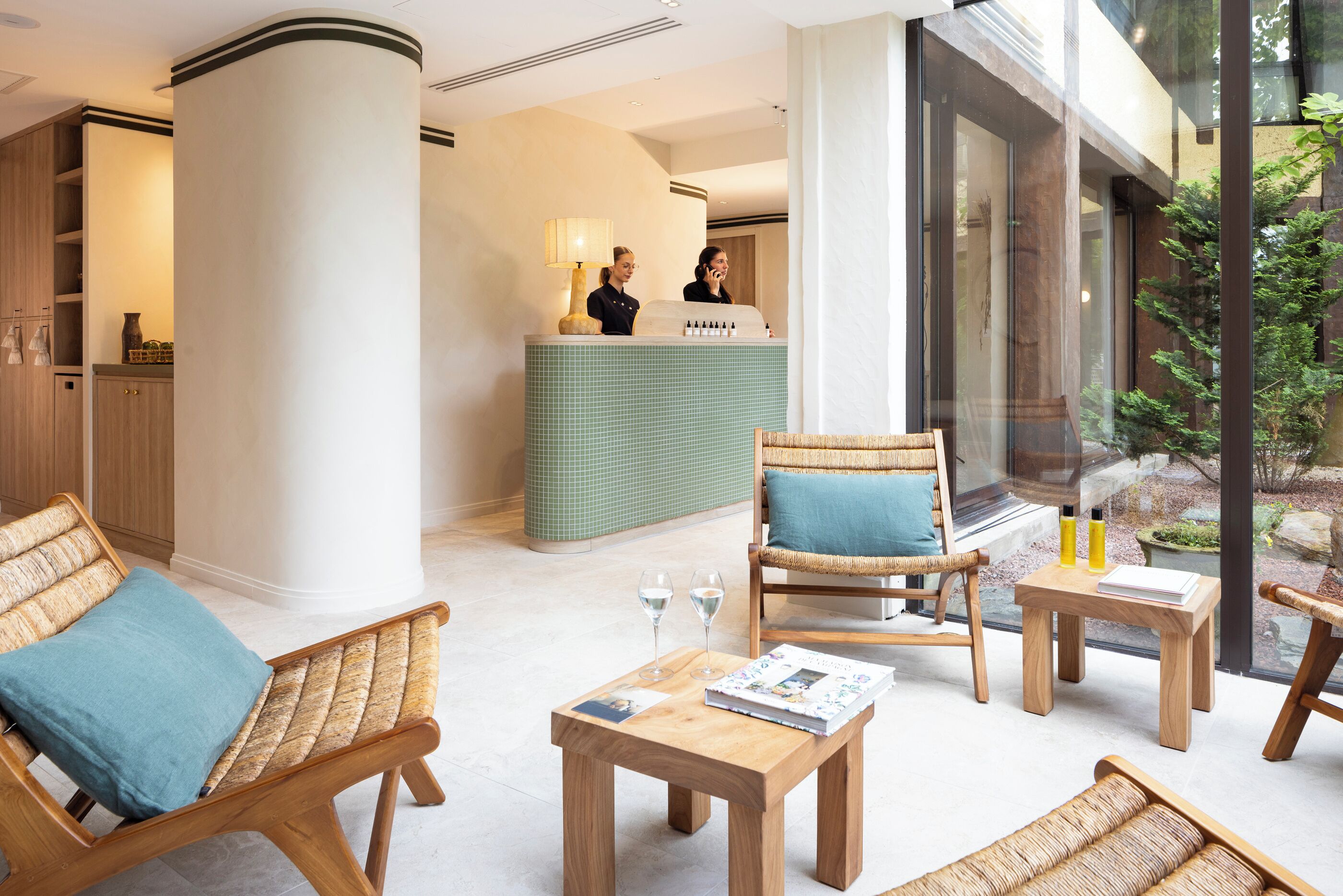 Un hall d’entrée avec un comptoir de réception, des fauteuils en osier, une petite table avec un magazine et une table basse en verre.