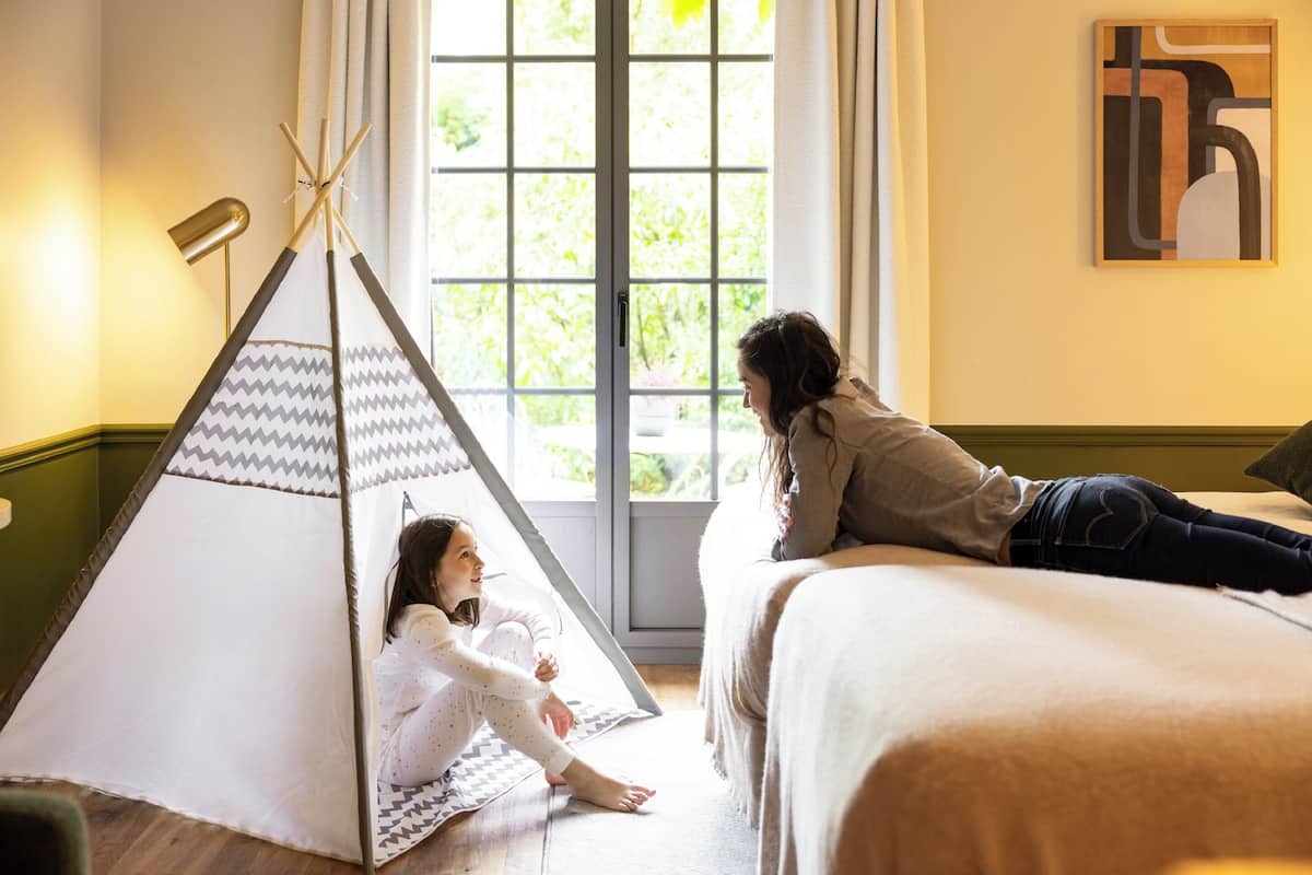 Een kamer met een bed, een raam met gordijnen, een schilderij aan de muur en een tipi.