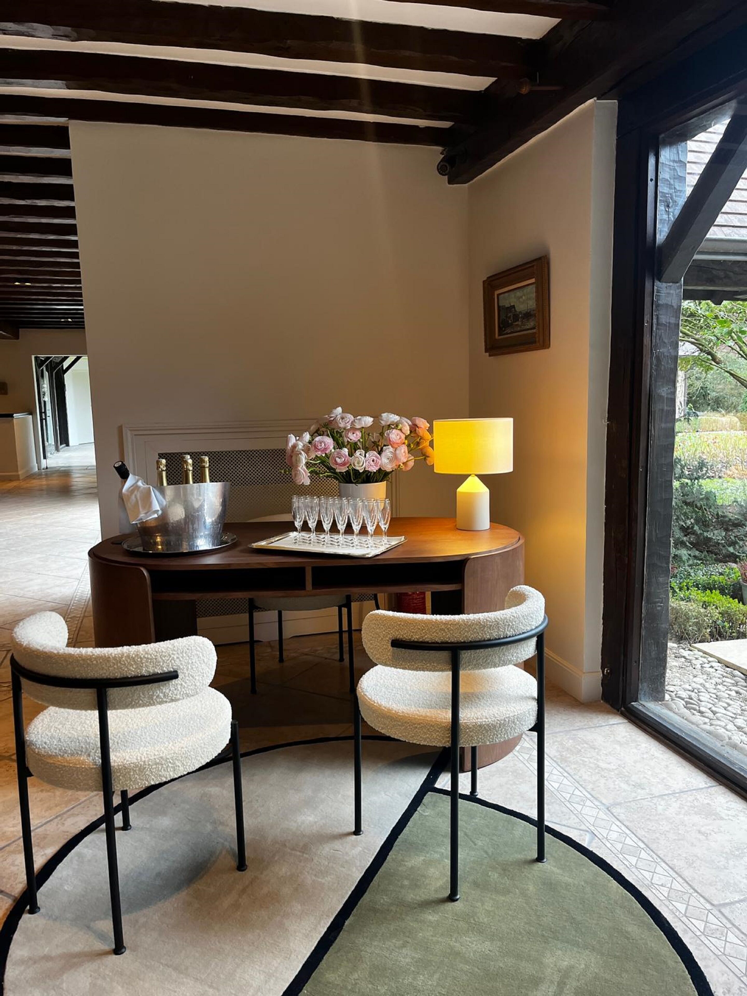 A dining area with a round table, two chairs, a vase of flowers, a wine bottle, and a candle.