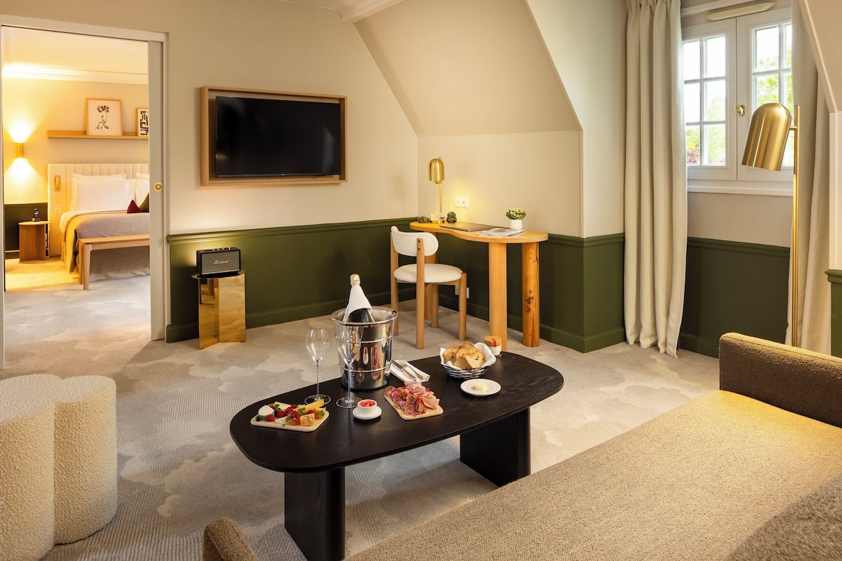 Een hotelkamer met een eettafel gedekt met eten en drinken, een bed, een televisie en een raam met gordijnen.