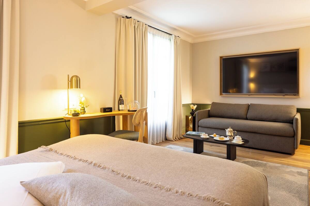 Een hotelkamer met een bed, een bank, een salontafel, een bureau met een lamp en een televisie.
