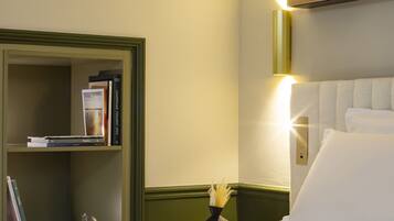 A hotel room with a bed, a bookshelf, and a wall-mounted light fixture.