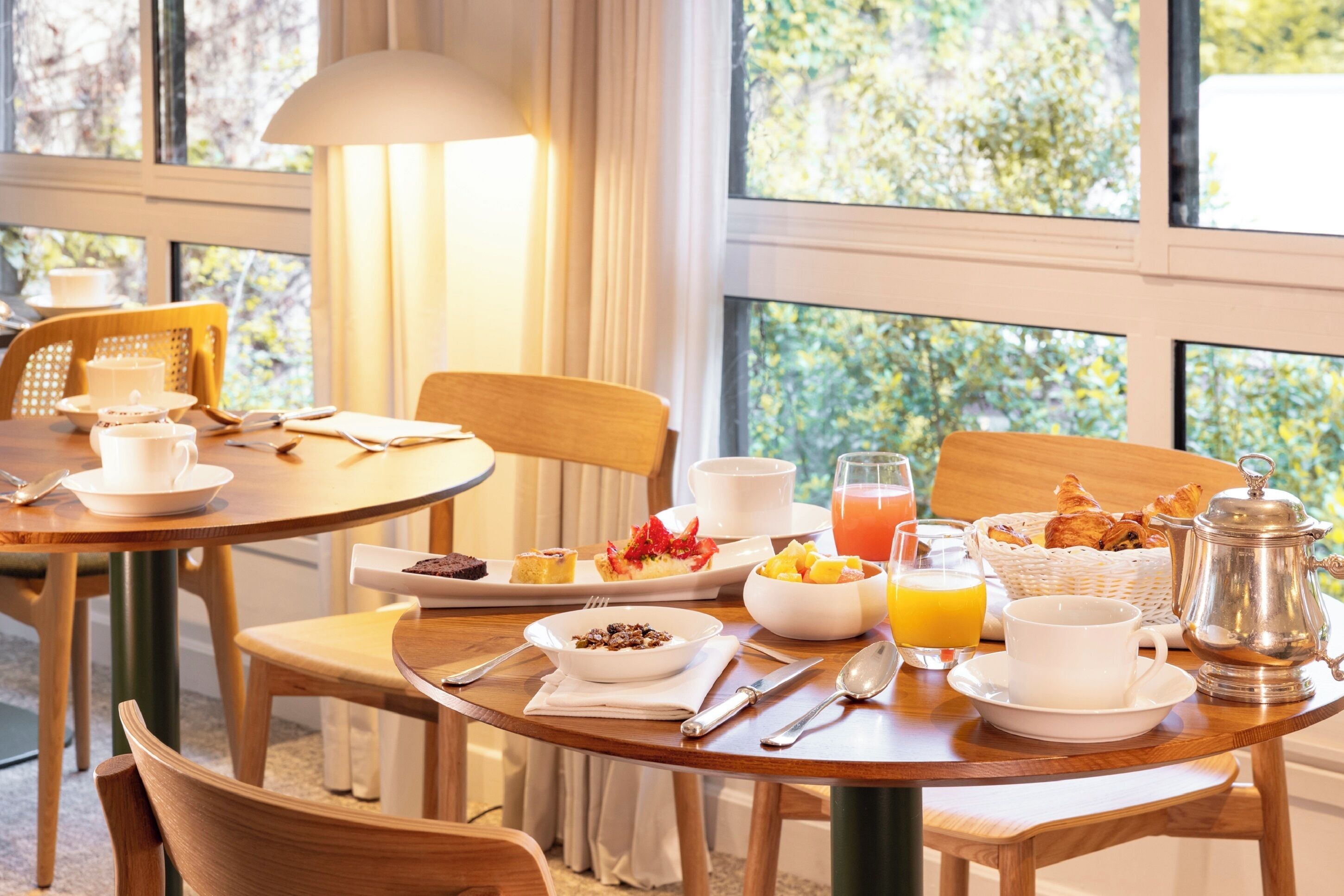 A breakfast setting with a table set for two, including plates of food, cups, and a coffee pot.
