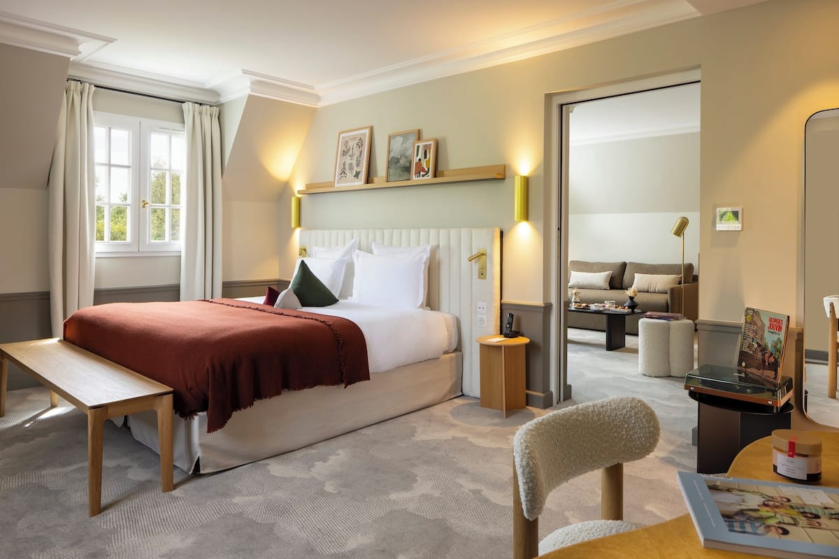 Een hotelkamer met een bed, nachtkastje, stoel en een kleintje tafeltje met een boek en een kaars.