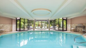 Ein großer, überdachter Pool mit Glaswänden, Liegestühlen und Blick ins Freie.
