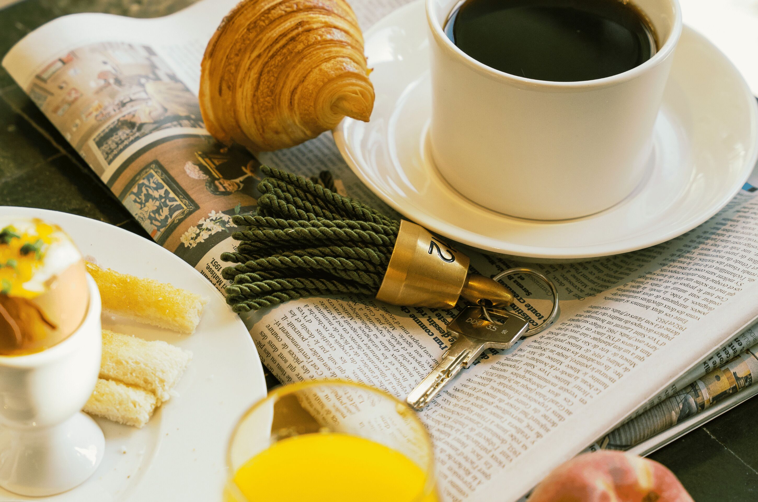 A breakfast setting with a croissant, coffee, and a newspaper.