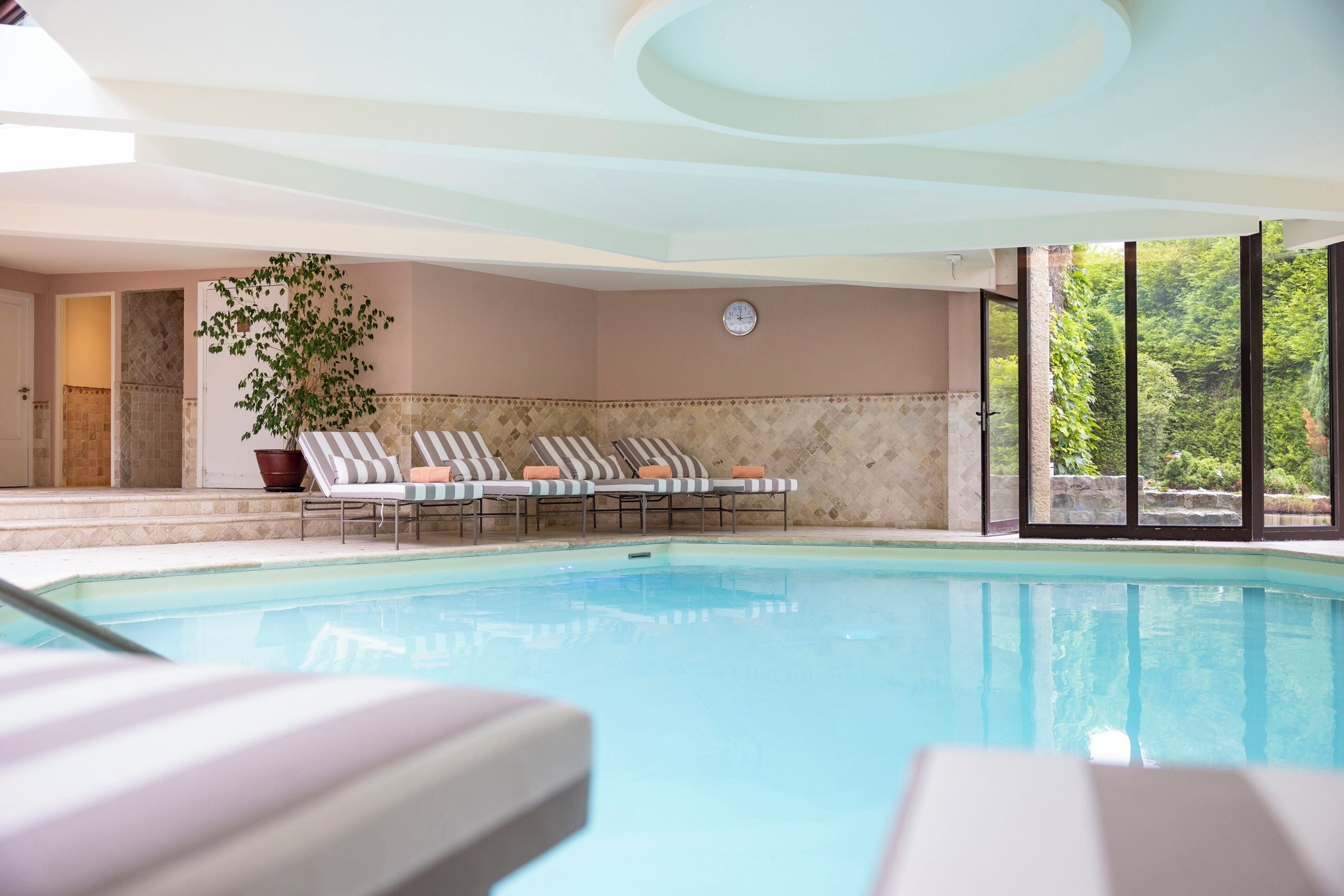 An indoor swimming pool with lounge chairs and a potted plant.