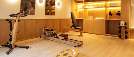 A room with a wooden floor, exercise equipment, a chair, and a shelf with towels and bottles.