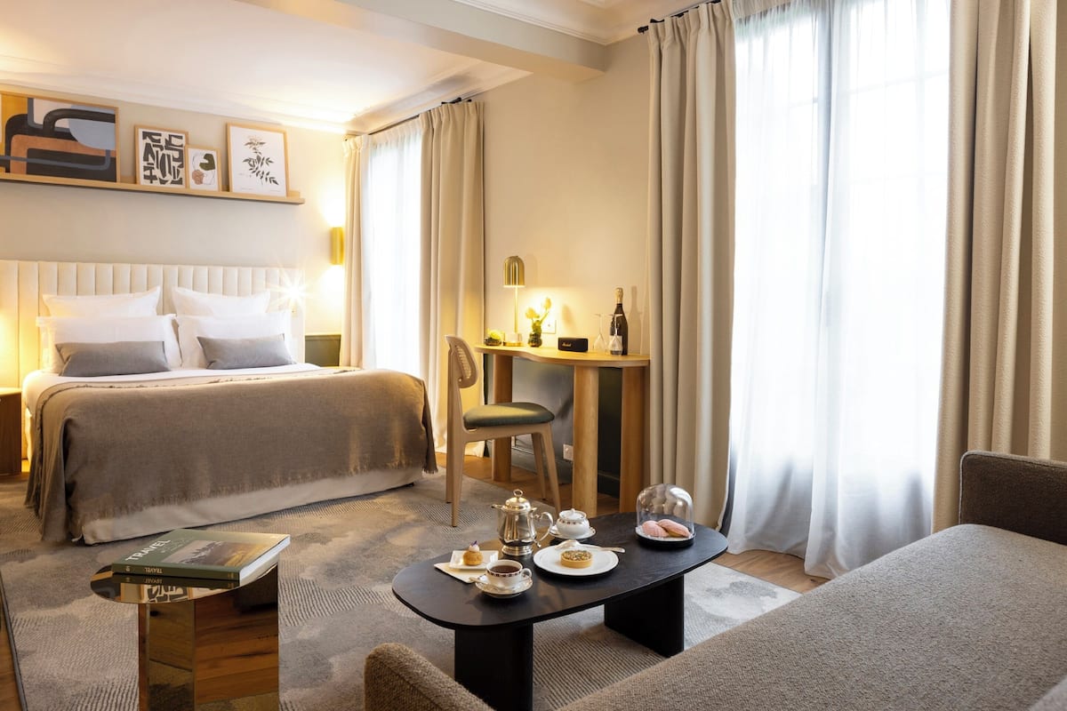 Une chambre d’hôtel équipée d’un lit, d’un bureau, d’une chaise et d’une table où sont disposés du thé et des pâtisseries.
