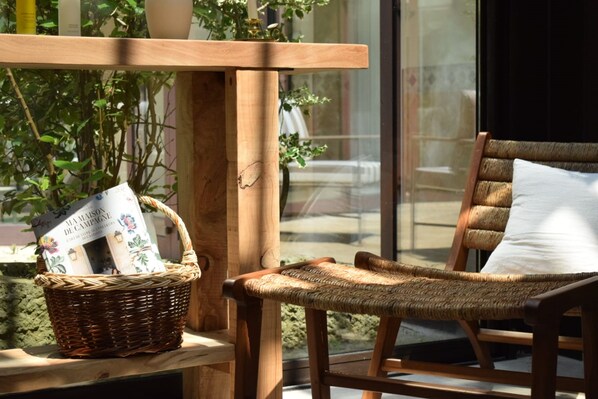 A wicker chair with a cushion, a wicker basket with magazines, and a wooden table.