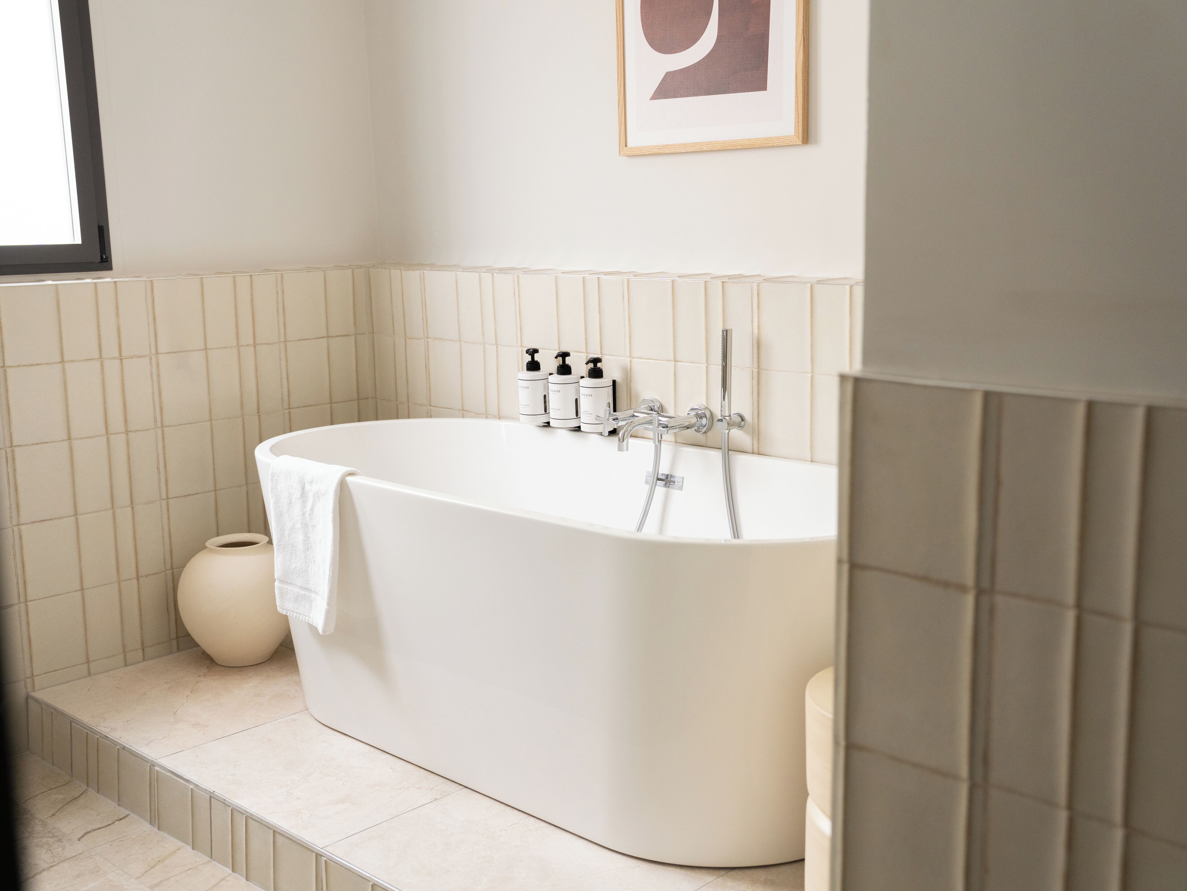 A modern bathroom with a freestanding bathtub, a towel, and a small round container.