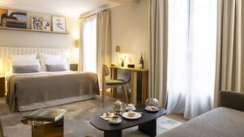 A hotel room with a bed, a desk, a chair, and a table set with tea and pastries.