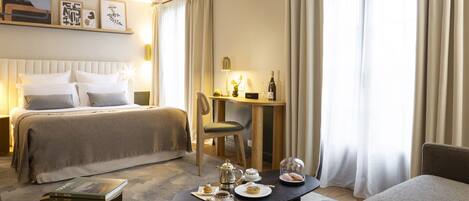 A hotel room with a bed, a desk, a chair, and a table set with tea and pastries.