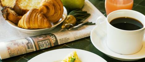 A breakfast setting with croissants, an apple, a glass of orange juice, a cup of coffee, and an omelette on a table.