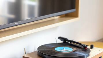 Tocadiscos sobre una mesa de madera con un disco de vinilo, un televisor montado en la pared y una revista sobre la mesa.