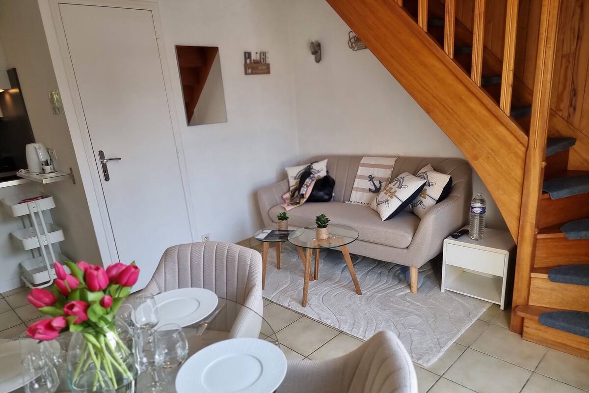Ein modernes Wohnzimmer mit einer Couch, einem Couchtisch und einem Essbereich mit Stühlen und einem Blumenstrauß.