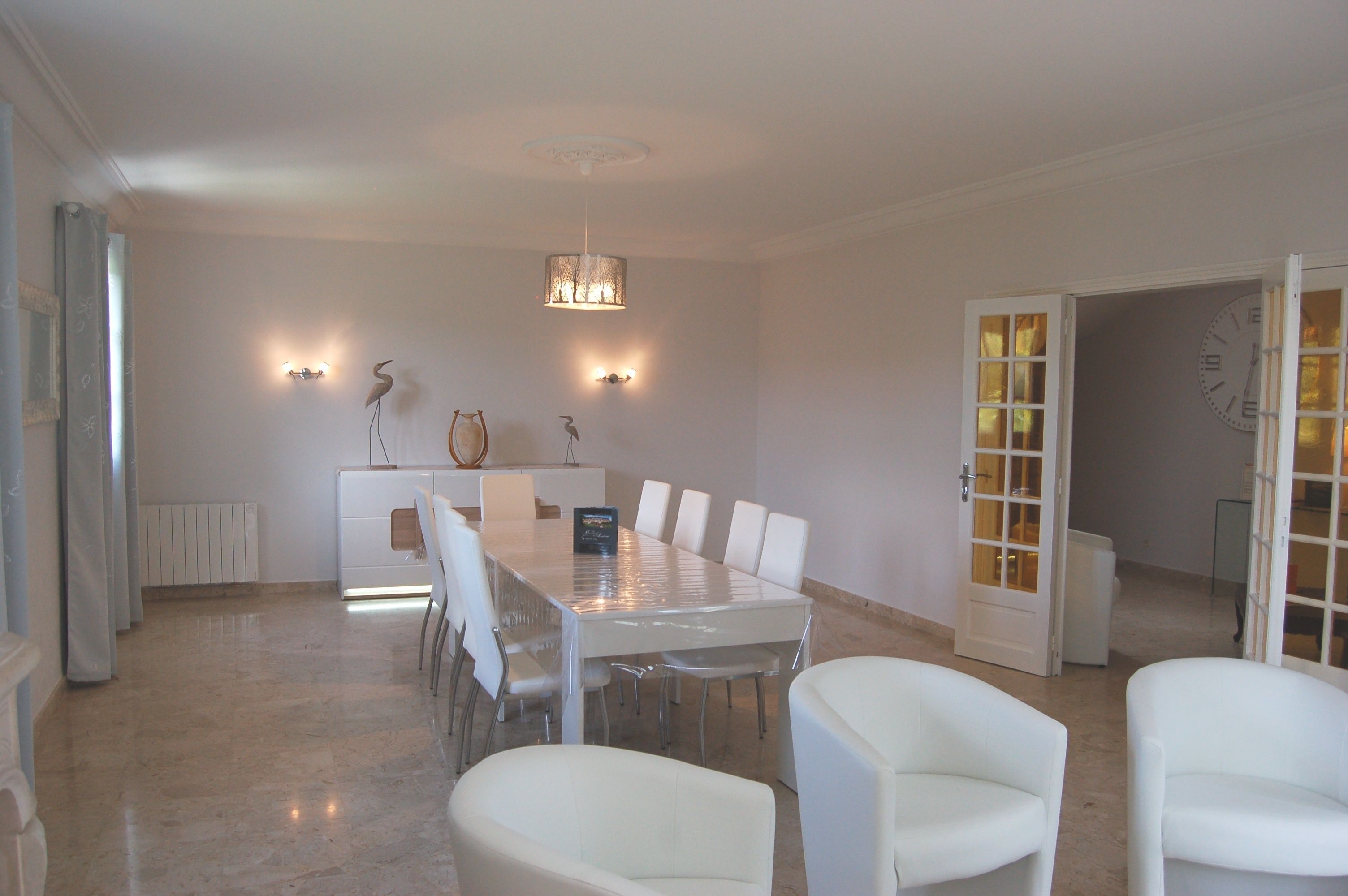 A dining area with a rectangular table surrounded by white chairs, a chandelier, wall-mounted lights, and a decorative bird sculpture.