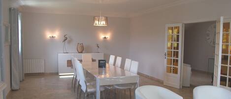 A dining area with a rectangular table surrounded by white chairs, a chandelier, wall-mounted lights, and a decorative bird sculpture.