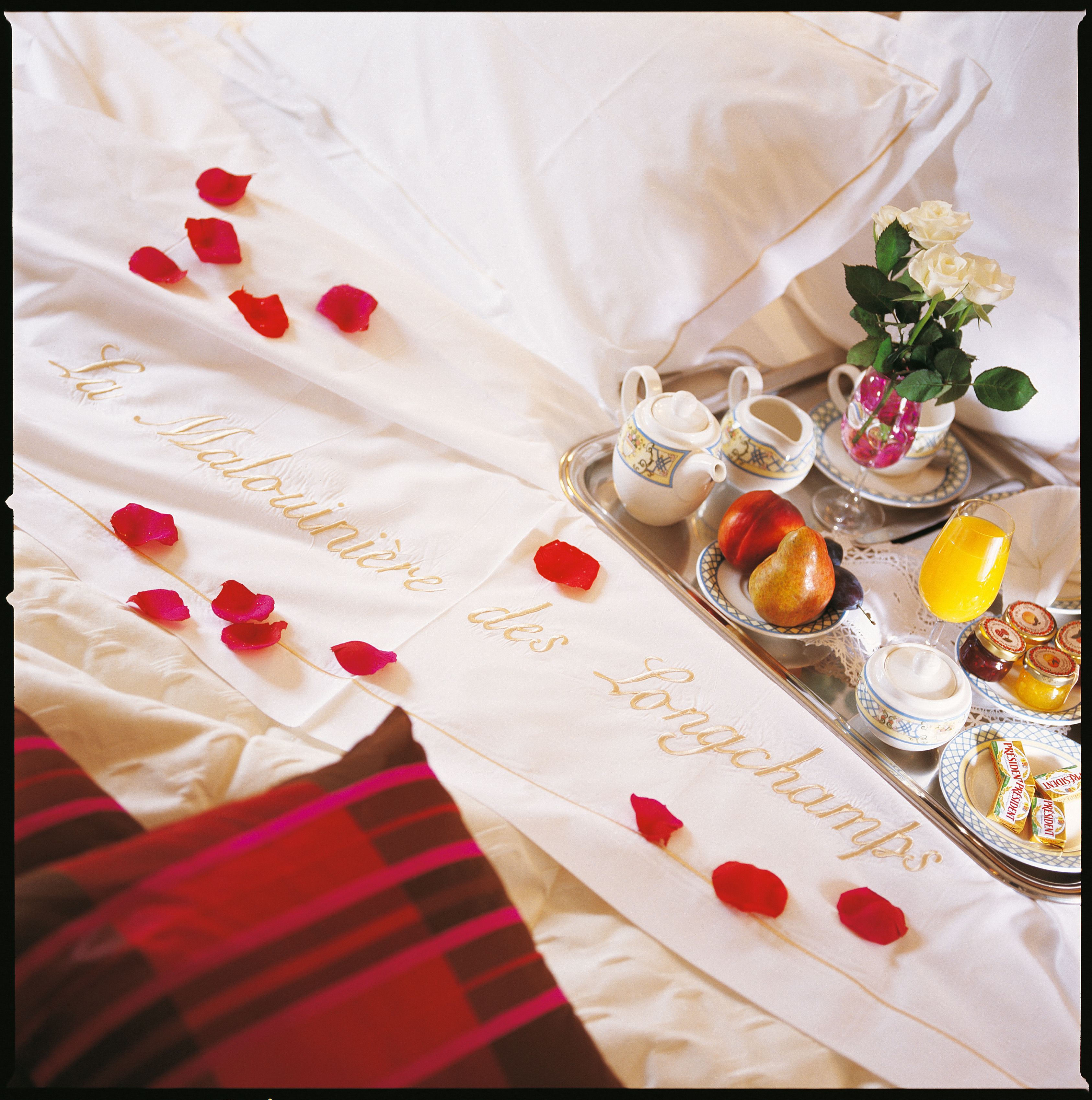 Un tavolo apparecchiato con una tovaglia bianca, un vassoio con teiere, tazze, un vaso con fiori e un piatto con frutta e marmellate.