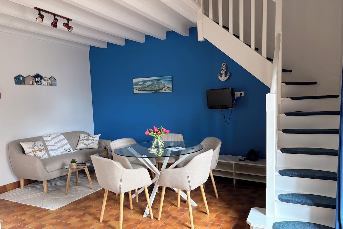 Ein Wohnzimmer mit blauer Wand, einem Glastisch, einer Couch und einer Treppe.