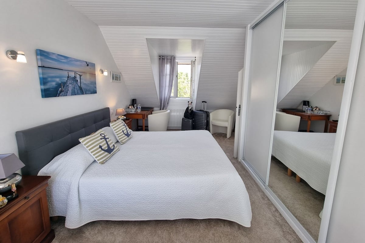 Ein Schlafzimmer mit einem Bett, Nachttischen, einem Schreibtisch, einem Stuhl, einem Fenster und einem Bild an der Wand.