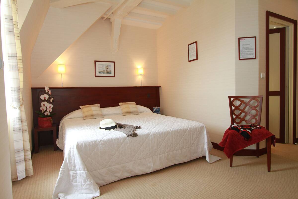 Ein Hotelzimmer mit einem großen Bett, einem hölzernen Kopfteil, zwei Wandlampen, einem Nachttisch, einem Stuhl und einer Tür.