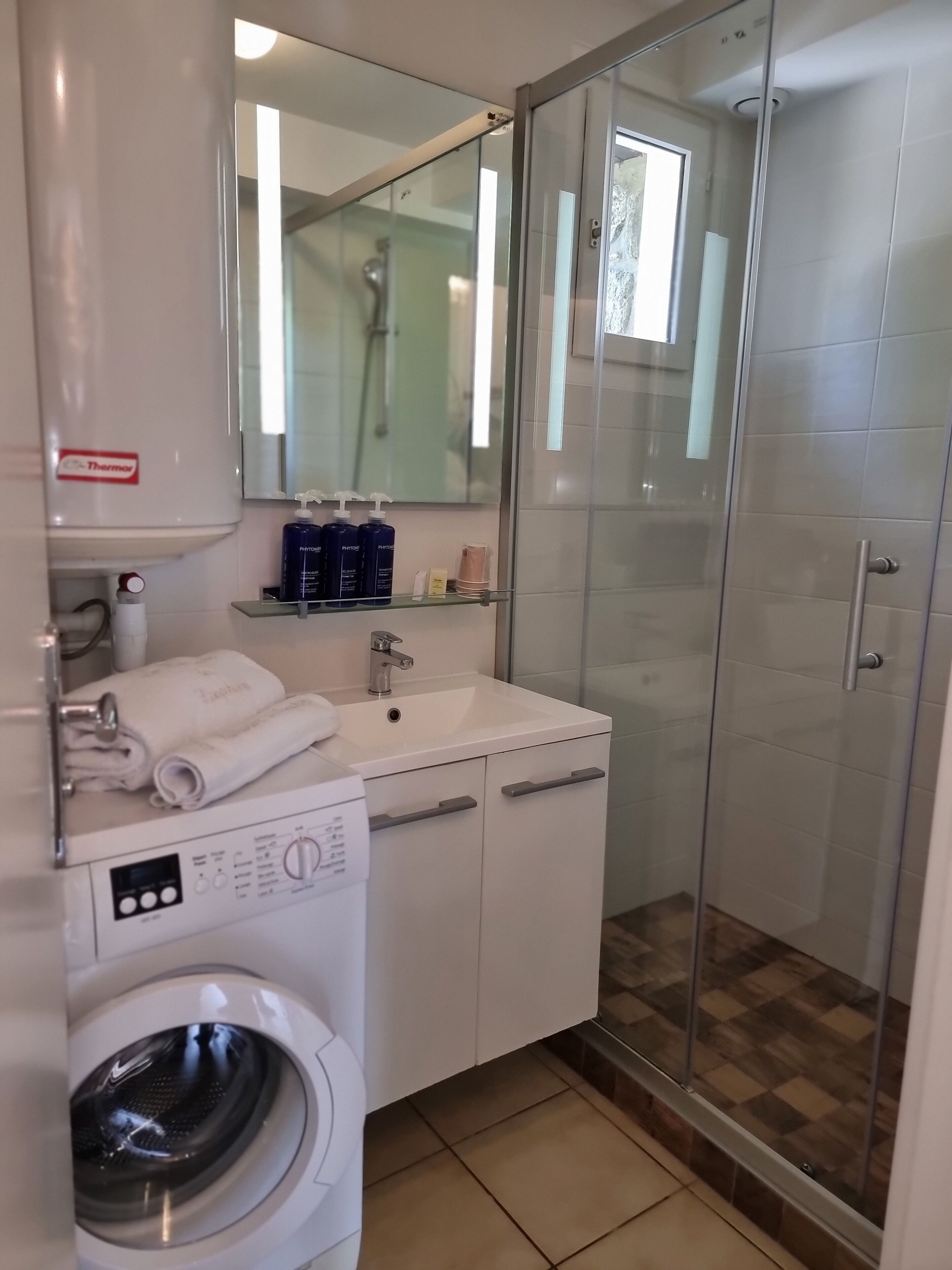 A modern bathroom with a washing machine, a sink, and a glass-enclosed shower.