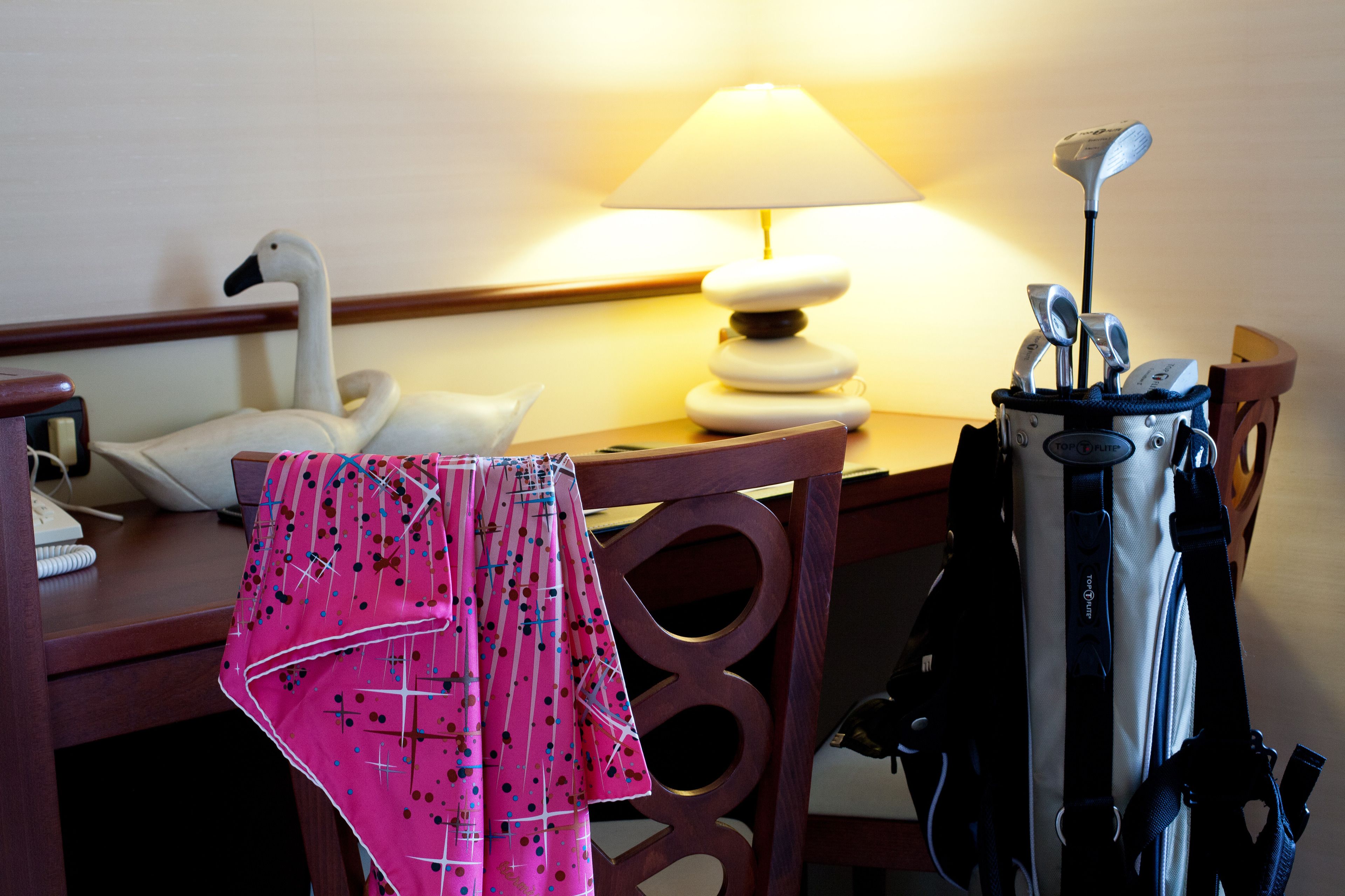 Une chambre d’hôtel décorée avec un cygne, une lampe, un sac de golf et un tissu à motifs roses.
