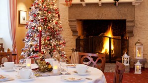 A Christmas tree in front of a fireplace, a dining table set with plates, cups, and a candle. - La Malouinière Des Longchamps (Saint-Jouan-des-Guerets)