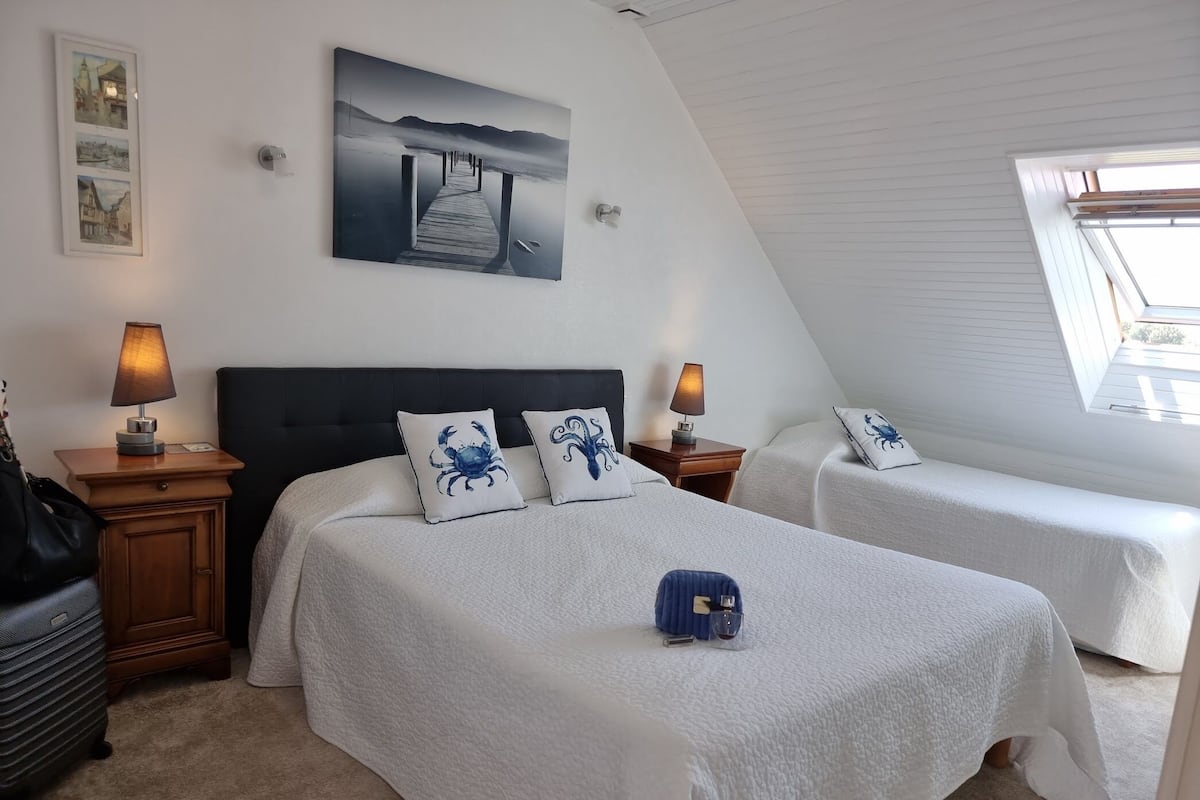 Ein Hotelzimmer mit zwei Betten, einem großen Gemälde, einer Lampe und Blick ins Freie.