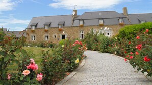 A stone building with a paved driveway and a garden with roses. - La Malouinière Des Longchamps (Saint-Jouan-des-Guerets)