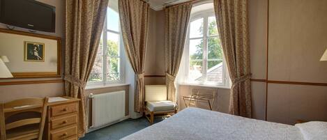 A bedroom with a bed, a desk, a chair, and two windows with curtains.