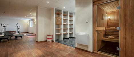 A spacious room with wooden flooring, a sauna, and a massage area with equipment.