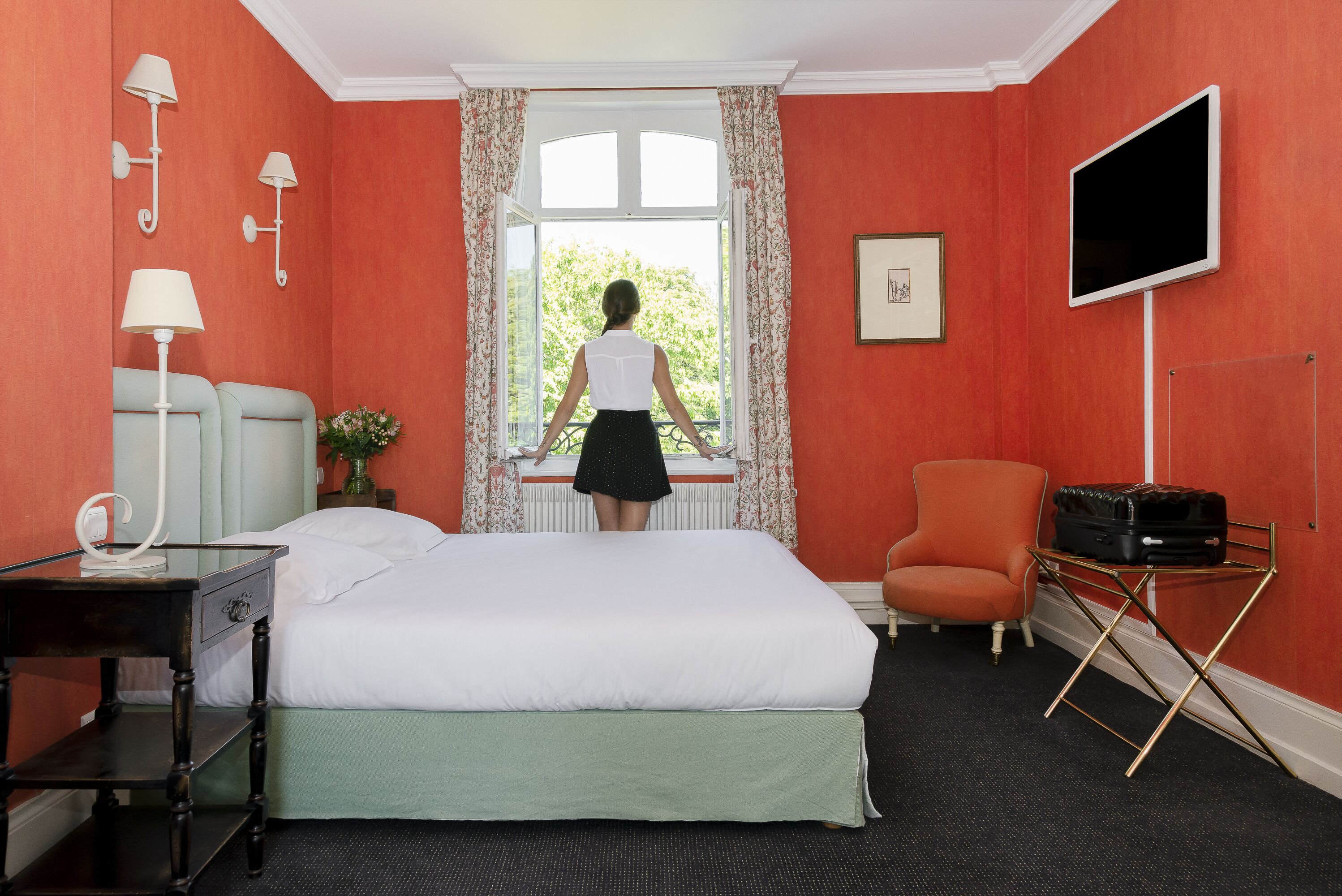Une chambre d’hôtel avec un lit, un bureau, une chaise, une télévision et une fenêtre avec des rideaux.