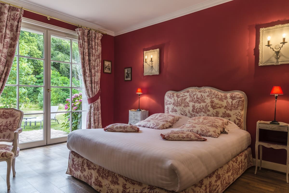 A bedroom with a large bed, a chair, a nightstand, and a window with curtains.